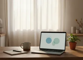 Laptop open on a kitchen table with a video call interface, mug, notepad, and houseplant in warm morning light